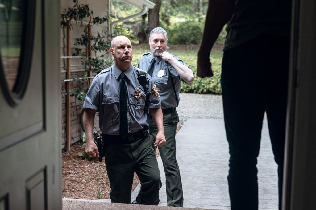 Two police officers approach a front door where a suspect is waiting for them.